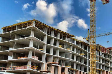İnşaat halindeki yeni bir konut iskeleti. Yeni bina. Beton paneller. İnşaat alanında vinç monte etmek. İnşaat devam ediyor. Konut yatırımı. Bulutlu mavi gökyüzü.