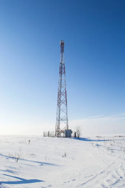 Mobile tower in a snow-covered white field against a blue sky. Data tower. Mobile communications and the Internet. Industrial equipment. Data transmission technologies. Winter season.