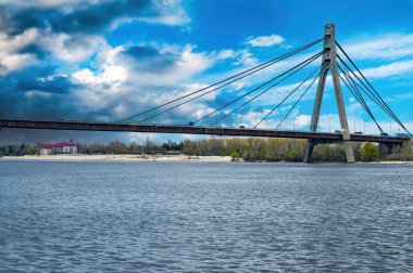 Kiev 'deki Dinyeper Nehri üzerindeki köprü bulutlu bir gökyüzüne karşı. Araba suyun üzerinden geçiyor. Nehrin üzerindeki köprü. Su akışı. Mavi gökyüzü. Gök gürültülü bulutlar. Geçmişi. Sanayi mimarisi.