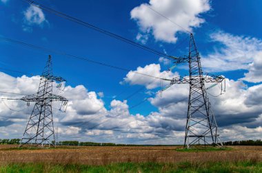 Kablolu yüksek voltajlı güç iletim kulesi. Yüksek voltaj hattı. Enerji endüstrisi. Enerji transferi. Mavi gökyüzü. Beyaz bulutlar. Tarım alanı. Bulutlu ufuk. İş için. Elektrikçi işi..