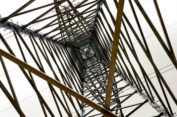 The metal structure of the frame of a high-voltage tower, view from the inside. View from bottom to top. Metal frame. Industrial background. Crossing of iron lines. Geometric abstraction.