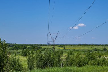 Enerji hatlarının kuleleri doğanın arka planında kablolarla çevrili. Elektrik enerjisinin yüksek voltajlı iletim kulesi. Endüstri ve doğa. Beyaz bulutlu mavi gökyüzü.