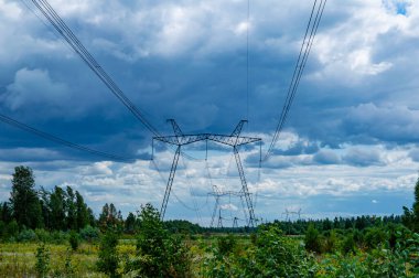 Enerji hatlarının kuleleri doğanın arka planında kablolarla çevrili. Elektrik enerjisinin yüksek voltajlı iletim kulesi. Endüstri ve doğa. Beyaz bulutlu mavi gökyüzü.