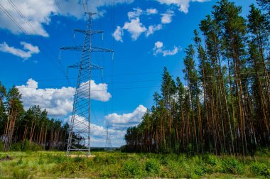 Enerji hatlarının kuleleri doğanın arka planında kablolarla çevrili. Elektrik enerjisinin yüksek voltajlı iletim kulesi. Endüstri ve doğa. Beyaz bulutlu mavi gökyüzü.