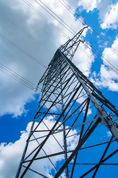 Enerji hatlarının kuleleri doğanın arka planında kablolarla çevrili. Elektrik enerjisinin yüksek voltajlı iletim kulesi. Endüstri ve doğa. Beyaz bulutlu mavi gökyüzü.