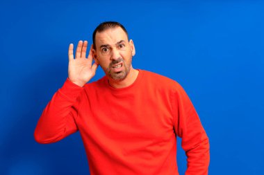 Dinleyen adam mavi arka planda elini kulağının yanında tutuyor. Yakışıklı adam birinin konuşmasını dinlemeye çalışıyor..