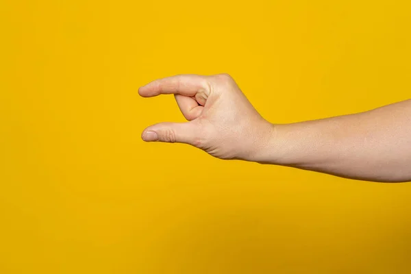 Sturdy mans hand making the small amount gesture isolated on yellow background