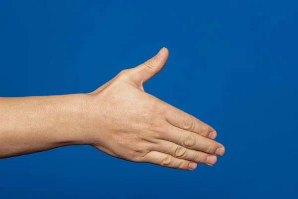 Man stretching out his hand to handshake isolated on a blue background. Mans hand ready for handshake