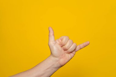 Middle age caucasian man hand over isolated yellow background gesturing hawaiian shaka greeting gesture, phone and communication symbol