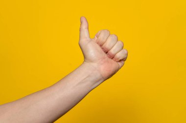 Thumb up hand sign. Mans hand showing thumb up, like, ok, approval, accept, okay, good, positive hand gesture. Isolated on yellow background.