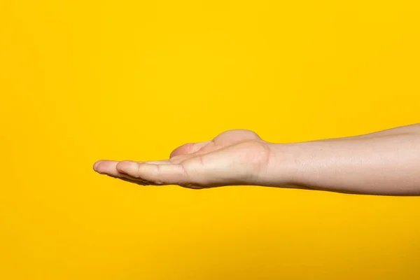 Strong hand of man with palm up presenting an imaginary product in advertising concept isolated on yellow background