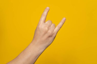 Male hand close-up on a yellow background shows hand gesture. Rocknroll. Isolate.