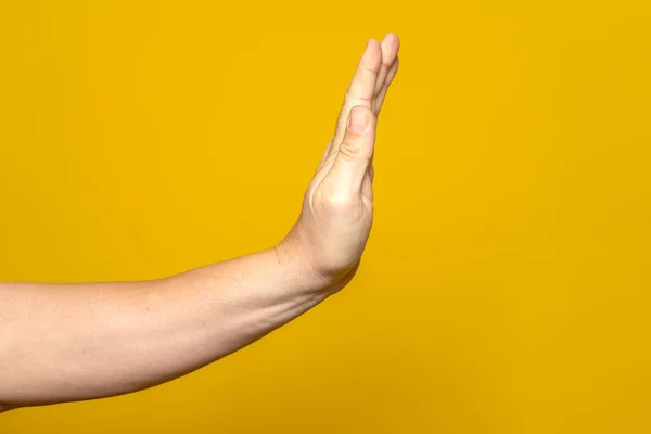 Hand of strong man making stop gesture to eliminate adversities and misfortunes isolated on yellow studio background