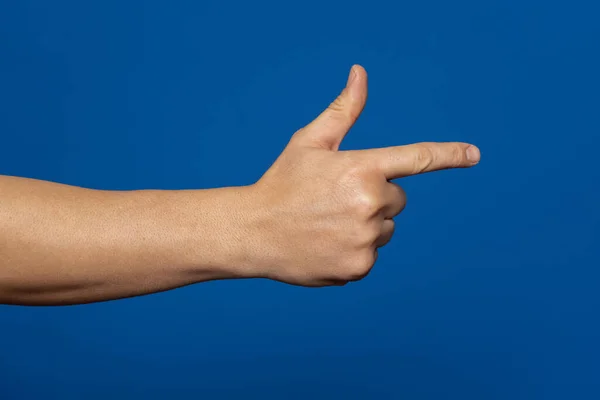 Mans hand making shooting, gesture. Hand gun gesture on isolated blue background. Mans hand pointing a finger.