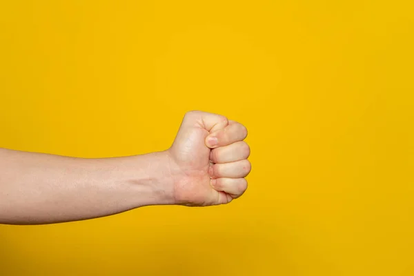 Strong mans hand in the form of a fist horizontally, isolated on yellow background. Fist ready to hit and hurt