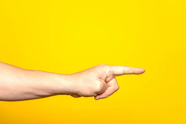 Mans hand pointing at something with the index finger, isolated on yellow background. Choice gesture. Side view.