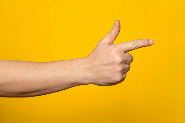 Mans hand making shooting, gesture. Hand gun gesture on isolated yellow background. Mans hand pointing a finger