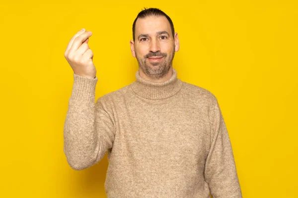 留着胡子的西班牙男人 身穿米黄色的毛衣 在镜头前微笑着做着一个意大利妈妈米娅的手势 与黄色背景隔离在一起 — 图库照片