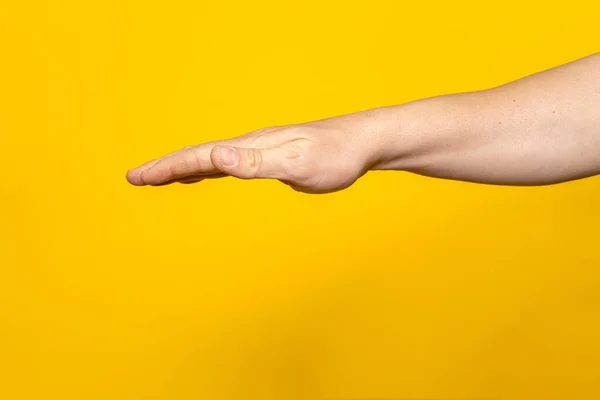 Strong mans arm with palm outstretched upside down isolated on yellow background