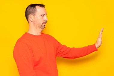 40 'lı yaşlarda sakallı İspanyol bir adam kırmızı bir kazak giyer. Profilde dikilirken durur, sarı arka planda izole olur.