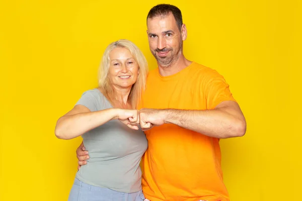 Partnership and collaboration work as a team. Caucasian woman and man making fist bumps and looking at each other, posing over yellow background, studio shot