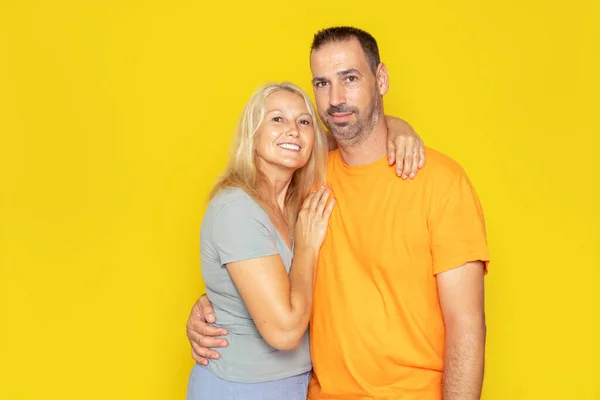 Caucasian real couple in their 40s embracing showing their love, isolated on yellow studio background