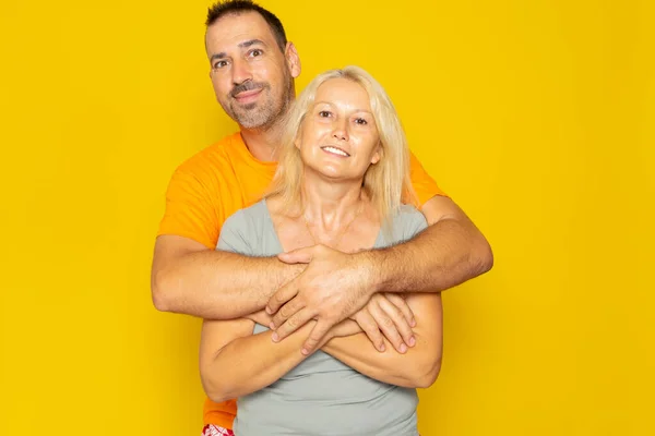 Caucasian royal couple in their 40s hugging each other in love and happy while smiling, isolated on yellow studio background
