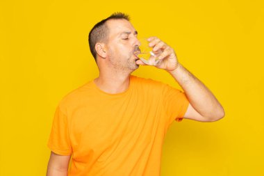 40 'larında sakallı, cam bardakta tatlı su içen, sarı arka planda izole edilmiş İspanyol bir adam.