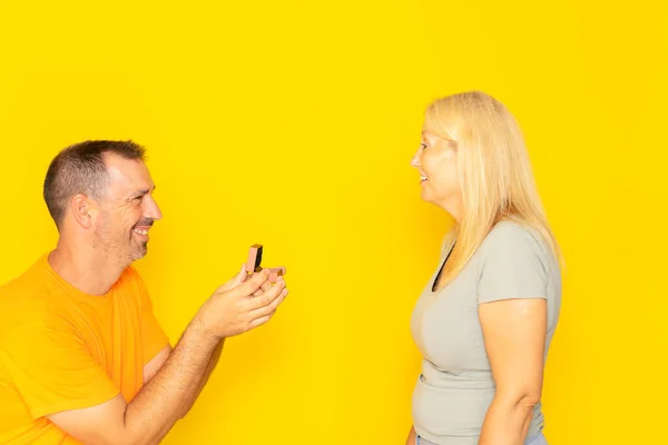 Man proposing to a woman who looks happy and surprised. Concept of love and marriage. isolated yellow background. Romantic concept, buying jewelry, wedding plans for bride and groom