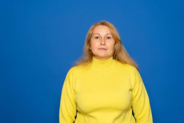Mavi arka planda sarı bir süveter giyen güzel, kahverengi saçlı, beyaz bir kadının yatay görüntüsü. Duygular konsepti