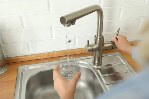 Woman pour water in glass from water mixer in kitchen