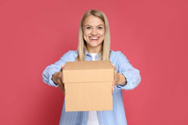 Teslimat ve hediye kavramı, genç bir kadın pembe arka planda bir kutu tutuyor.