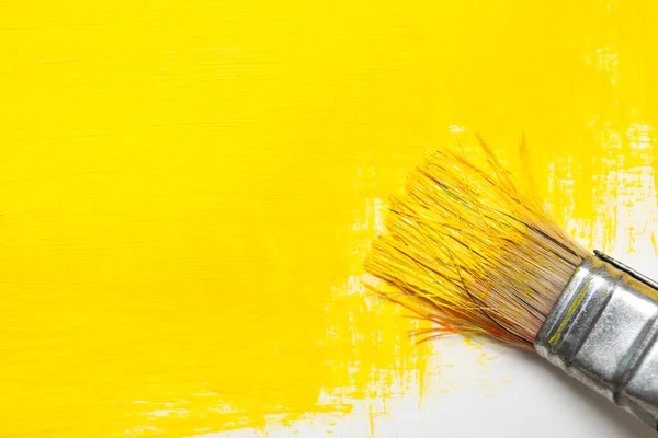 Paint brush with yellow paint and white background with yellow paint