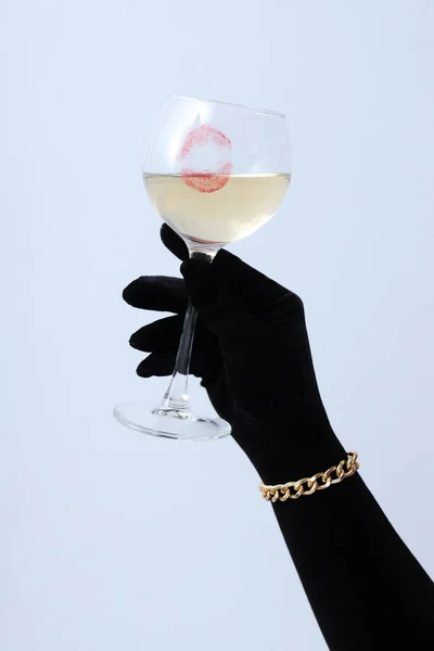 Female hand in black glove holds glass of wine with kiss on white background