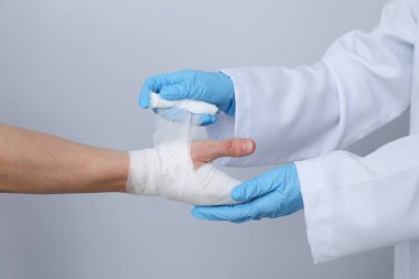 Concept of help during an injury, doctor wrapping hand in bandage on white background