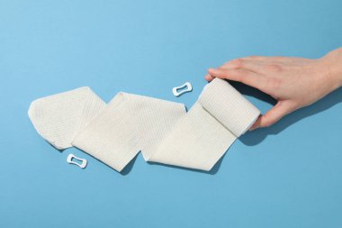 Concept of help during an injury, female hand and elastic bandage on blue background
