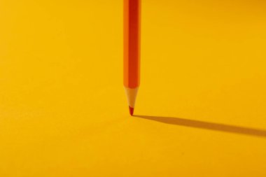 Orange pencil on yellow background, close up
