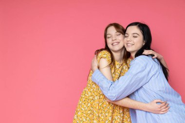 Two beautiful young women, sisters - twins on pink background