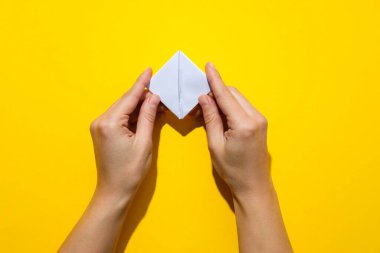 Female hands fold paper boat on yellow background