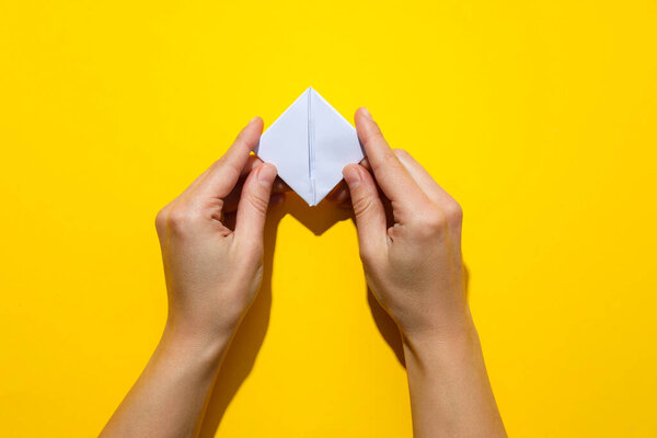 Female hands fold paper boat on yellow background