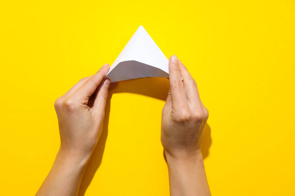 Female hands fold paper boat on yellow background