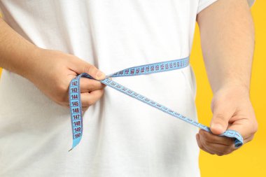 Concept of weight loss, fat guy with measuring tape on yellow background