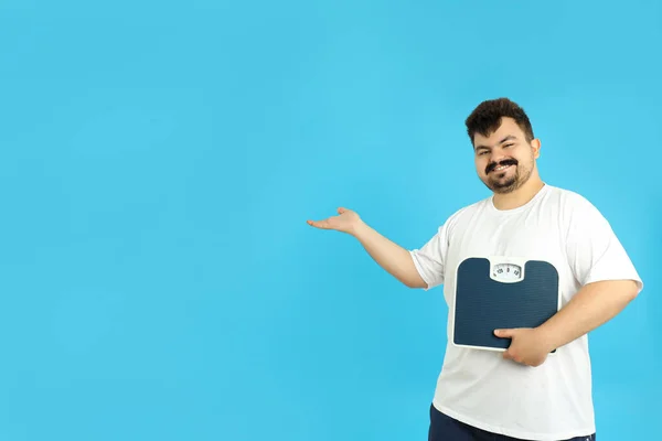 Concept of weight loss, young man with scales on blue background