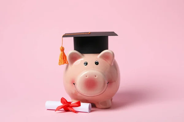 stock image Piggy bank with graduation hat and degree scroll on pink background