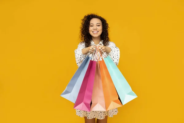 Young woman with shop bags on yellow background