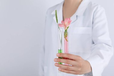 Kadın, arka planda çiçekli test tüpleri tutuyor.
