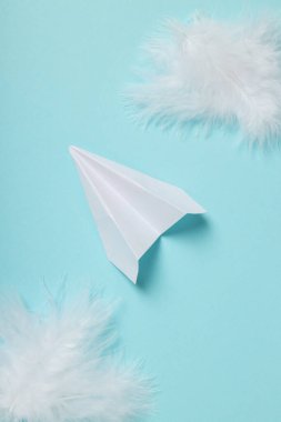 Kağıt uçak ve tüyler mavi arkaplanda