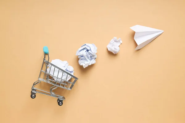 Shop cart, paper balls and paper plane on beige background