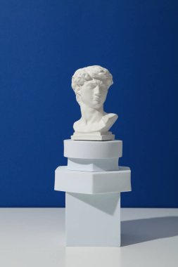 Geometrik şekiller ve antik kafa beyaz masada mavi arkaplanda