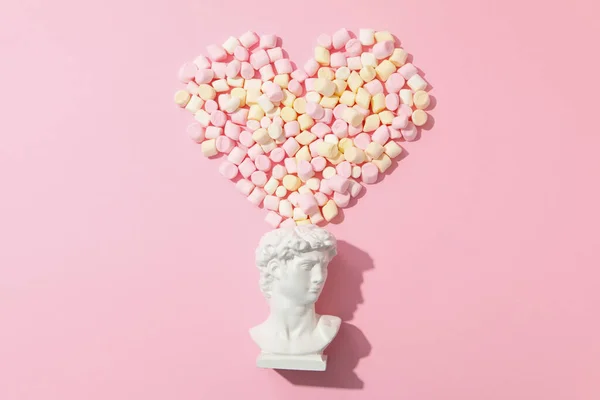 Heart made of marshmallow and ancient head on pink background